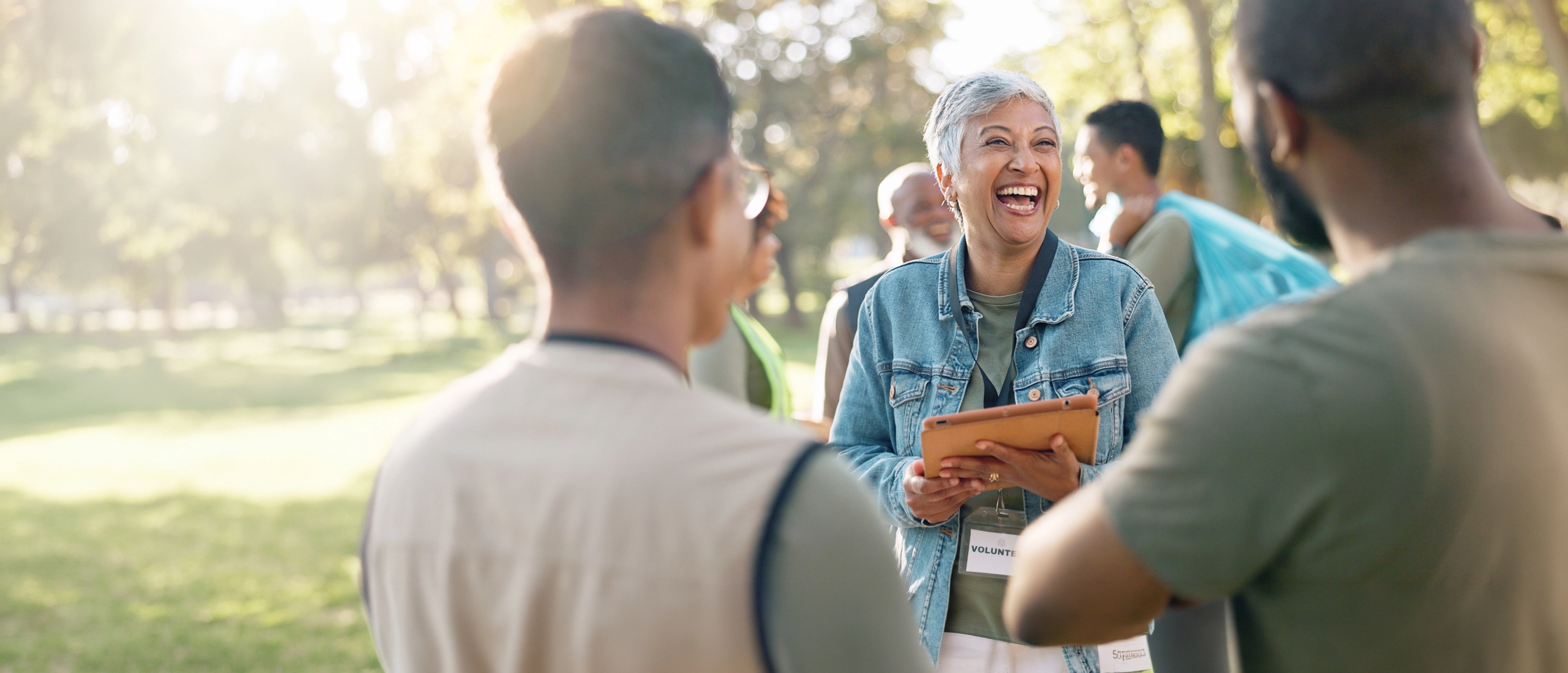 Laughing volunteer holding a tablet, talking with her team outdoors in a park